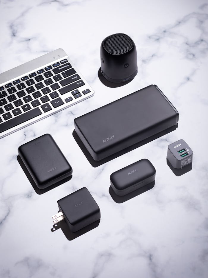 about-us-02 A collection of sleek black tech gadgets on a marble surface, featuring a keyboard and wireless speaker.