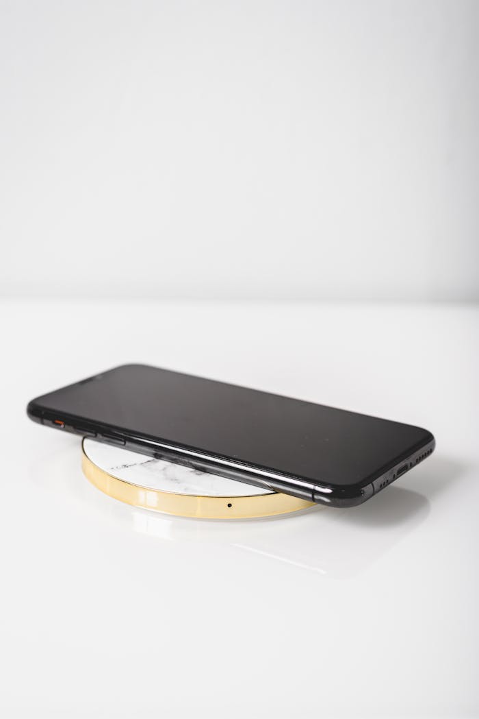 A sleek black smartphone placed on a wireless charger with a modern white background.