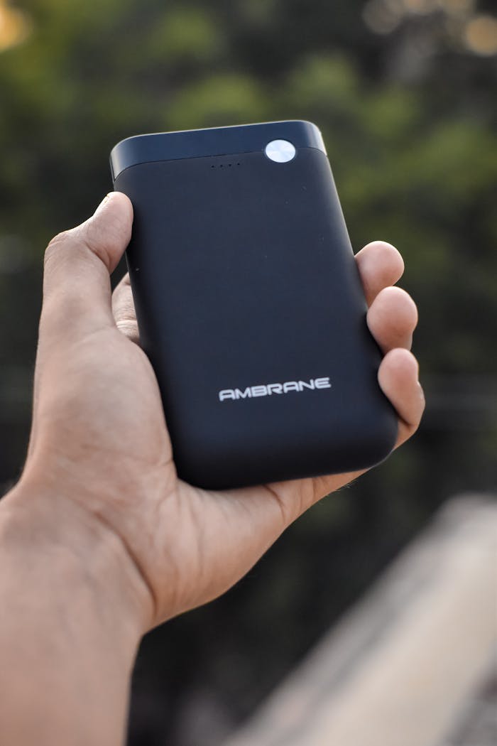 Close-up of a hand holding an Ambrane power bank outdoors. Ideal for tech visuals.